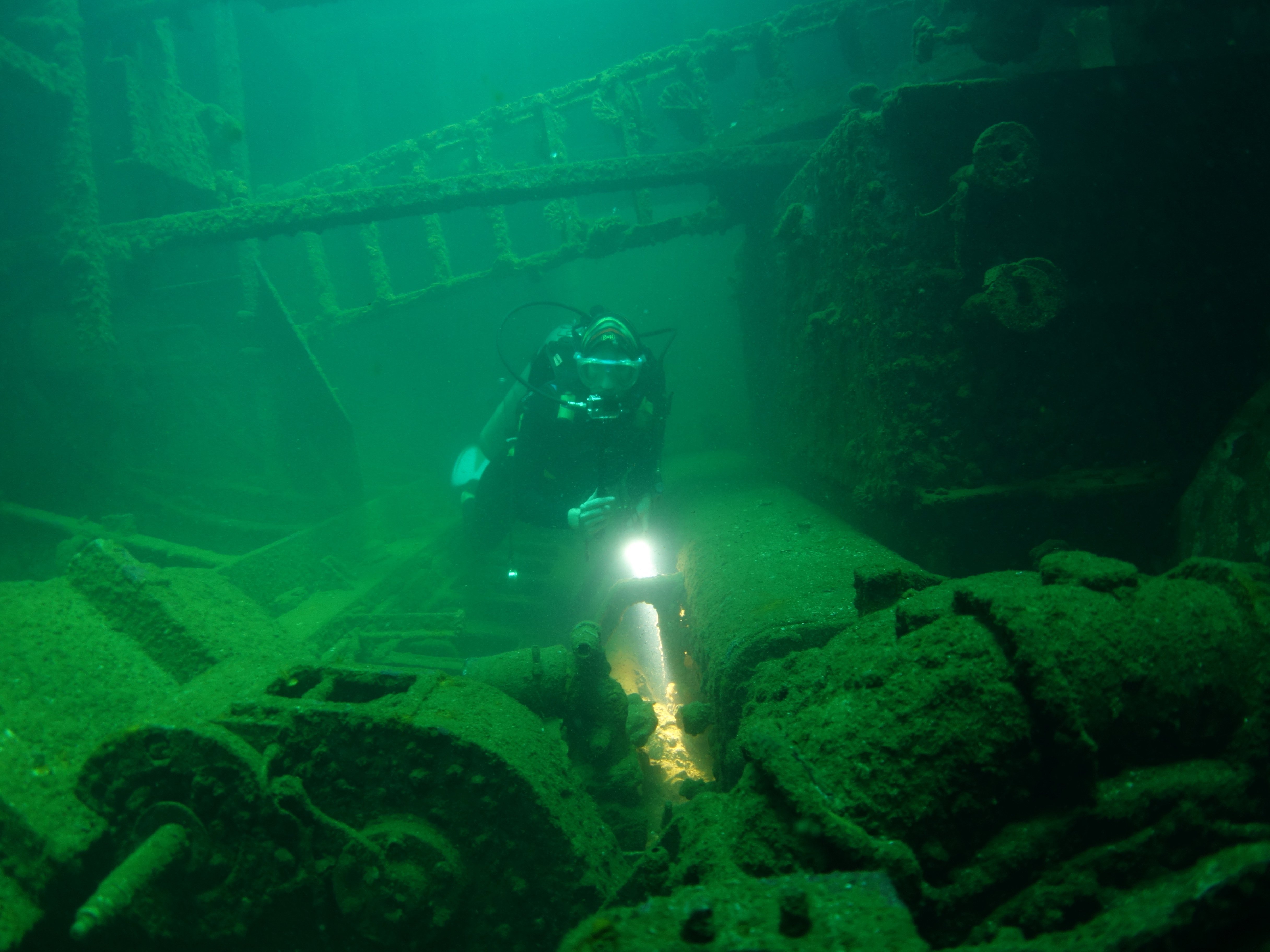 Ein Taucher taucht über einem Wrack am Meeresboden.
