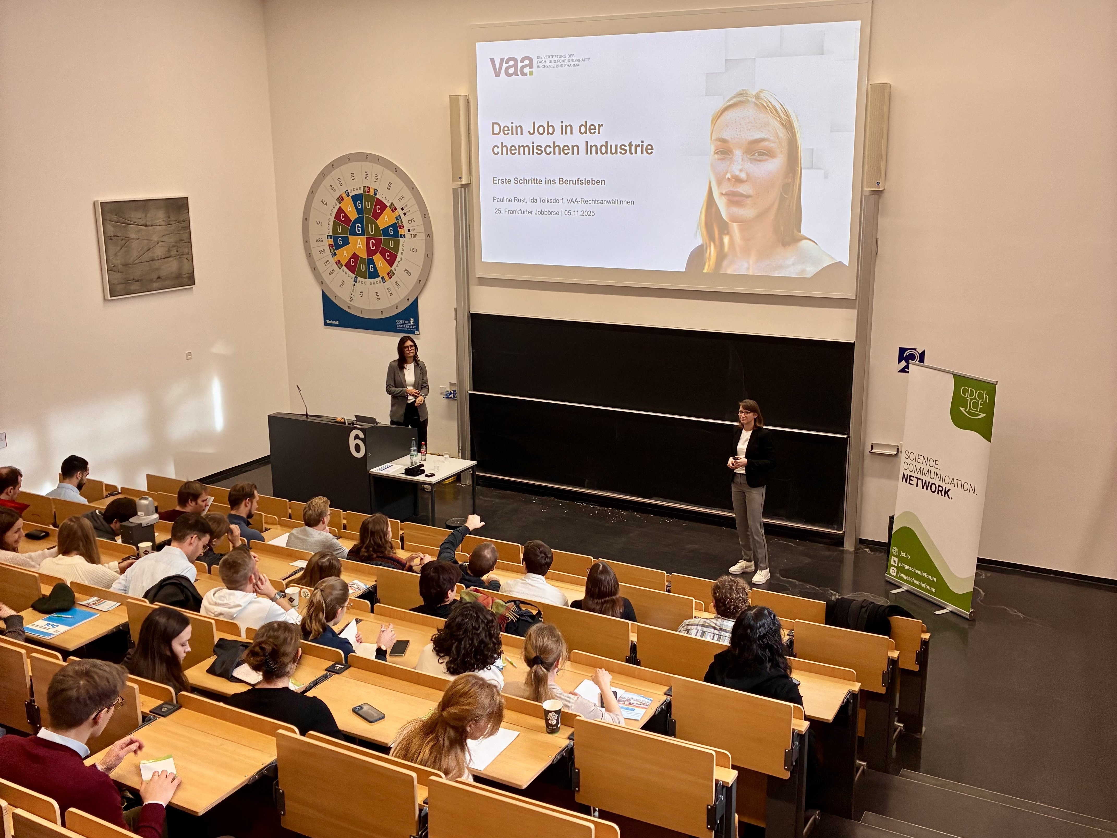 Ein Hörsaal mit Studierenden und Promovierenden. Vorne unter der Leinwand mit dem VAA-Vortrag die beiden Juristinnen Pauline Rust und Ida Tolksdorf.