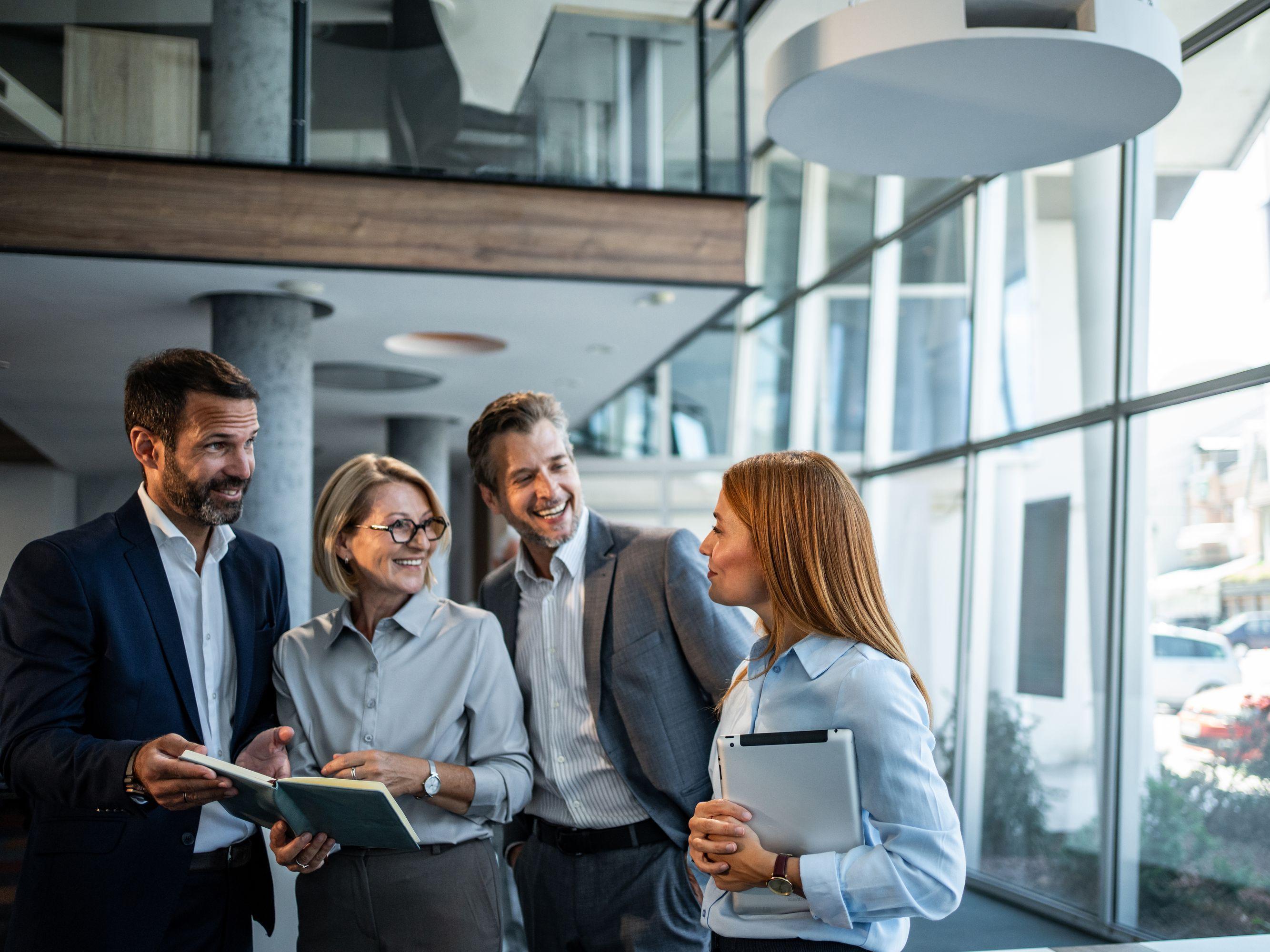 Eine Gruppe von Beschäftigten, zwei Männer und zwei Frauen im Business-Look, in einem Bürogebäude.