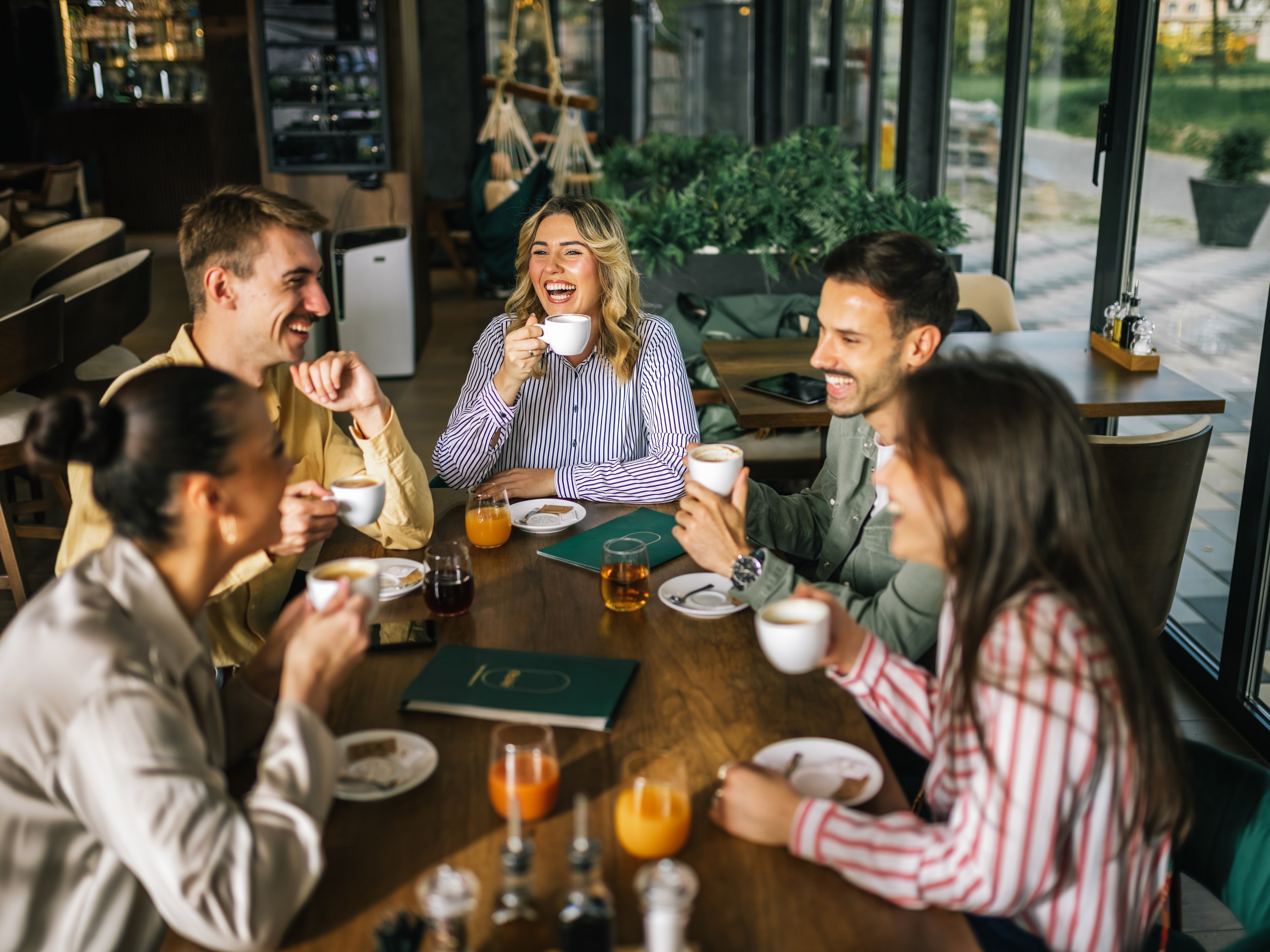 Eine Gruppe junger Menschen sitzt gut gelaunt an einem Tisch in einem Café.