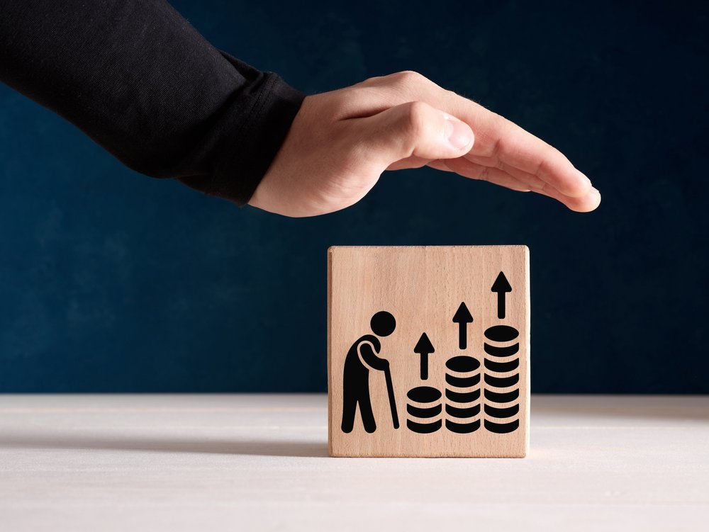 Eine Hand schützend über Bauklötzen mit einem Strichmännchen, das am Stock geht. Vor ihm drei Münztürme, die größer werden mit Pfeilen darüber.