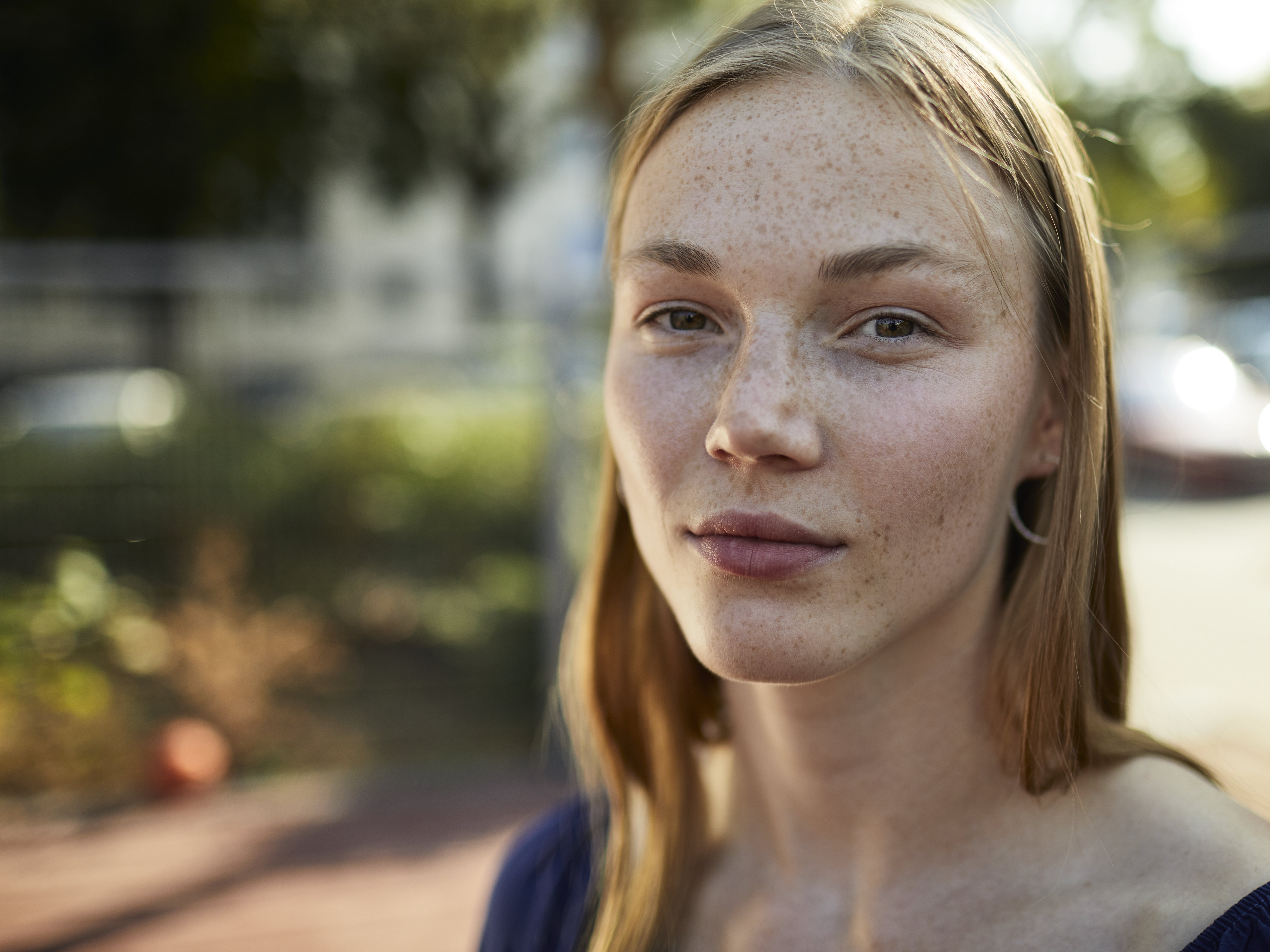 Nahaufnahme einer jungen Frau, die direkt in die Sonne schaut. Im unscharfen Hintergrund warmes Wetter.