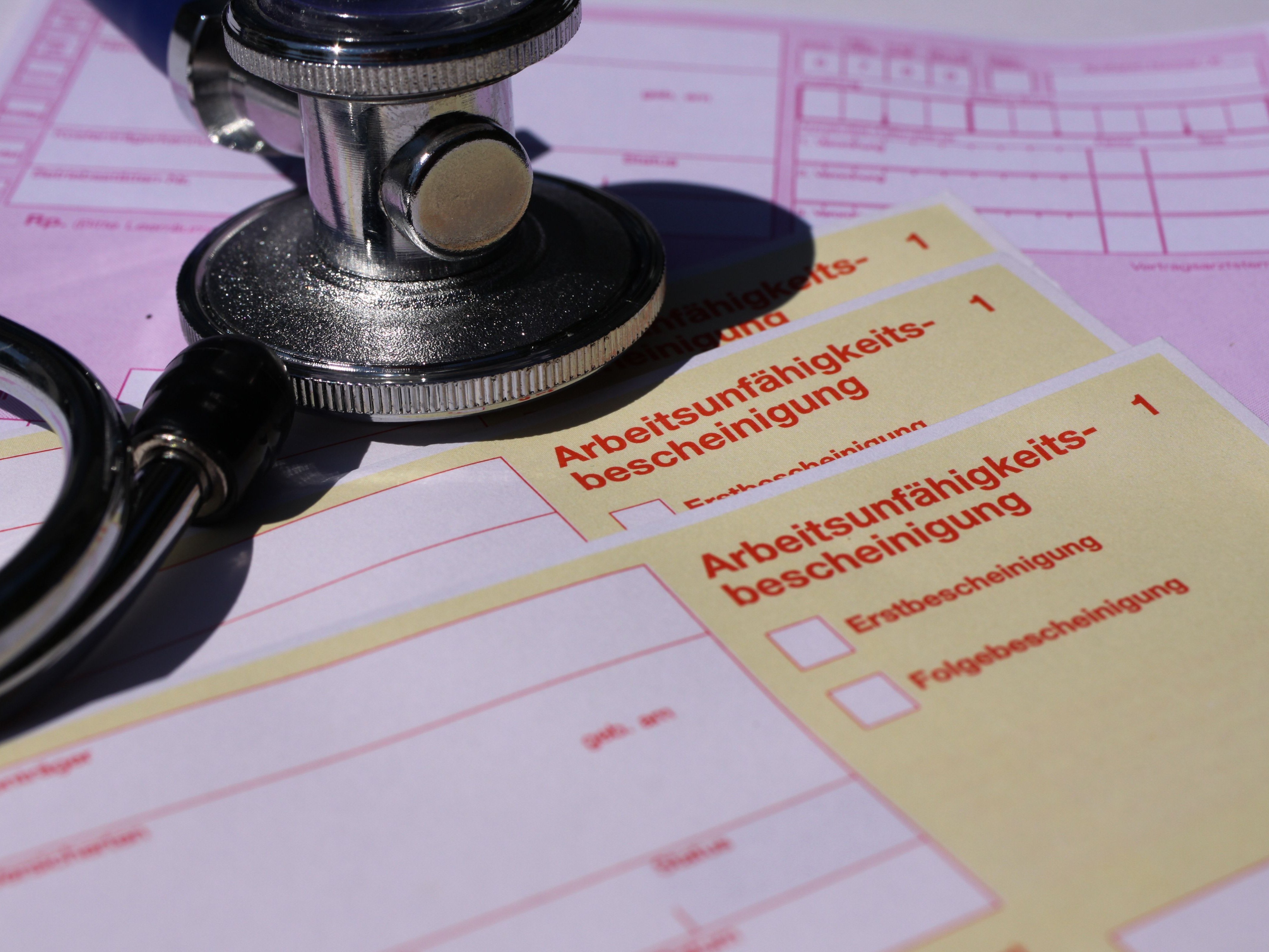 Das Foto zeigt ein Stethoskop, das auf einem Stapel Arbeitsunfähigkeitsbescheinigungen liegt.