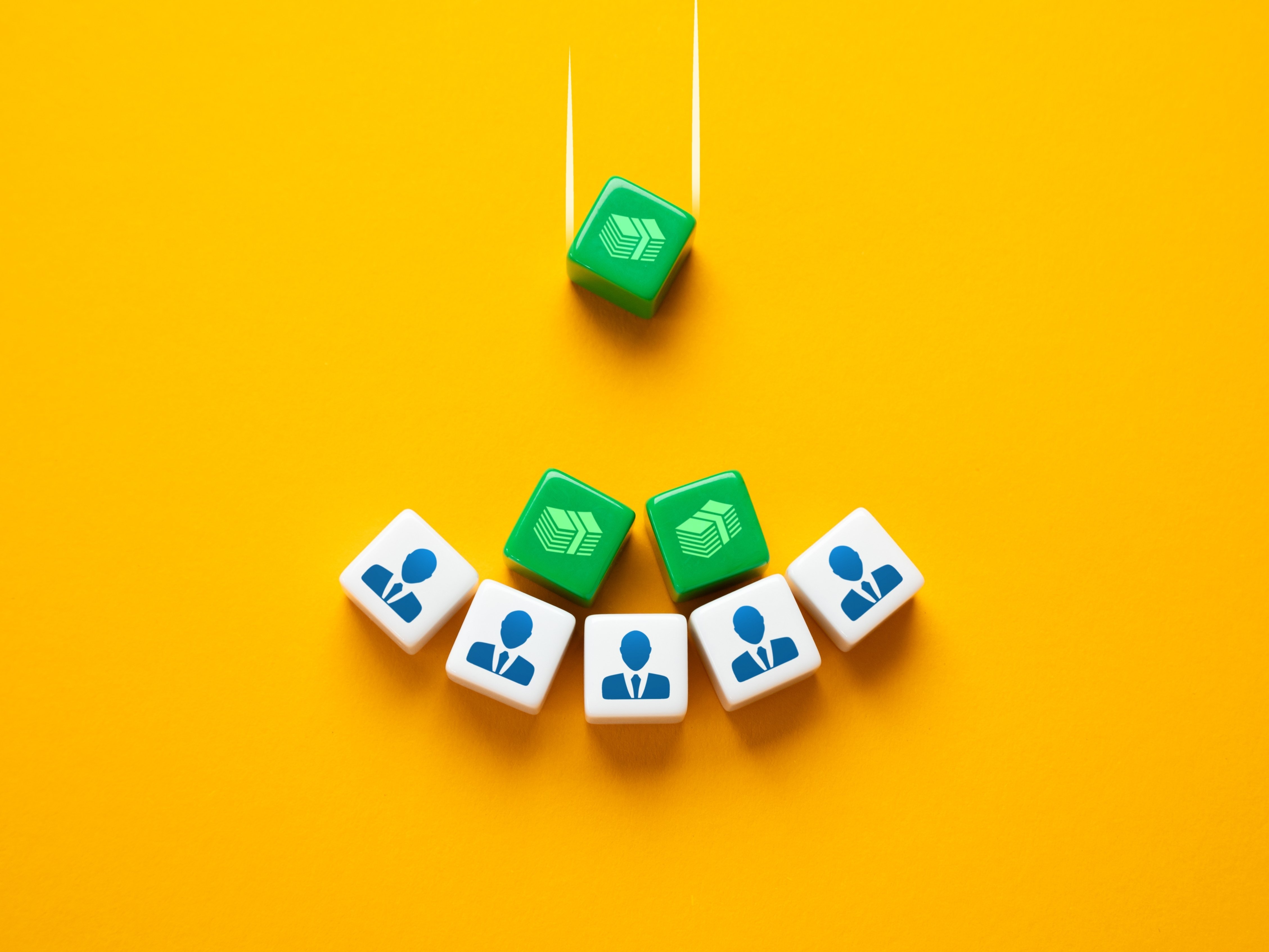 Auf gelbem Untergrund drei grüne Würfel mit Geldschein-Piktogramm und fünf weiße Würfel mit Piktogramm von Mann im Anzug. Die grünen Würfel fallen auf die weißen.