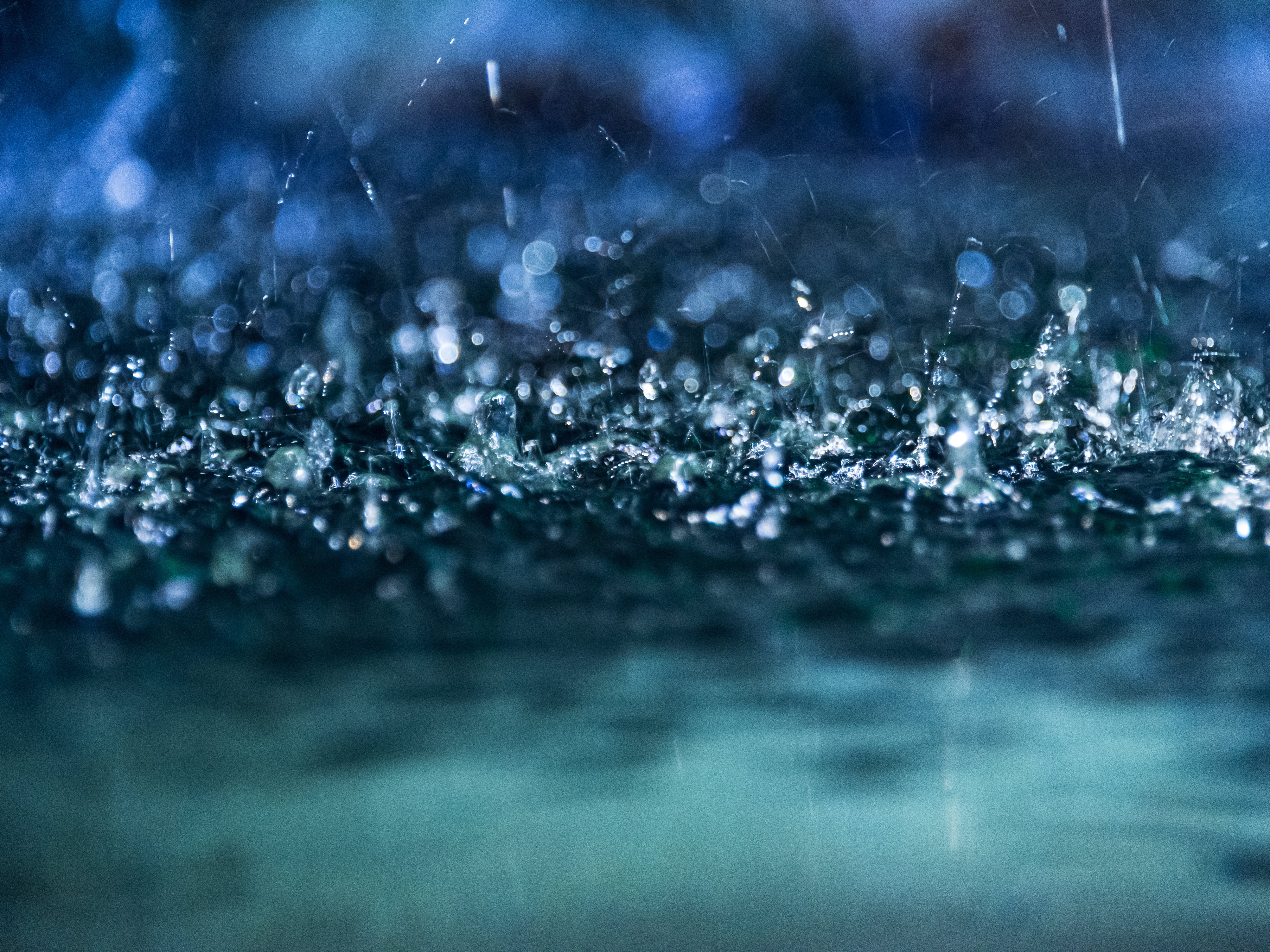 Nahaufnahme von Regentropfen, die in einer Pfütze aufkommen.