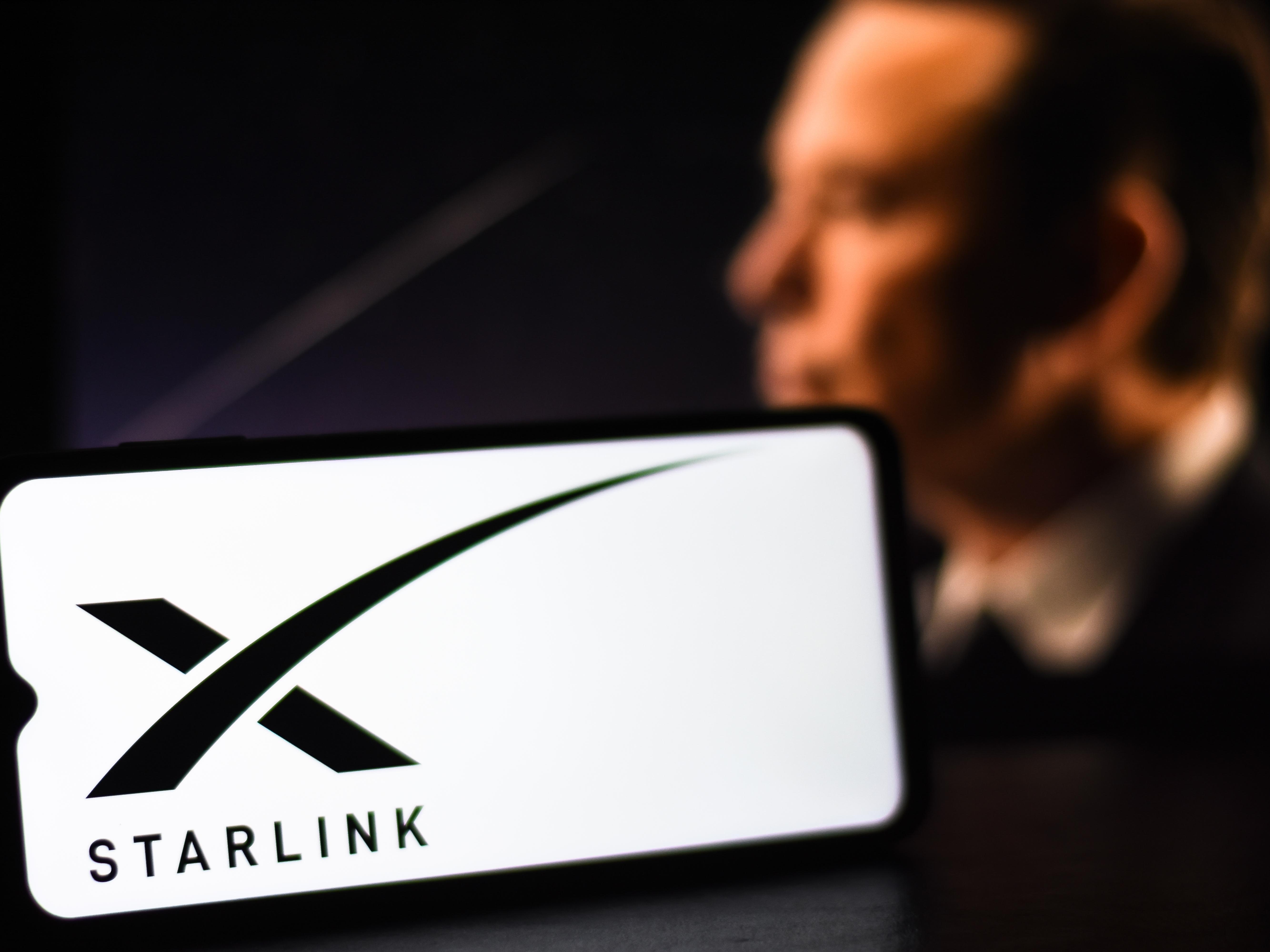 Starlink-Logo im Vordergrund mit Elon Musk im Hintergrund.