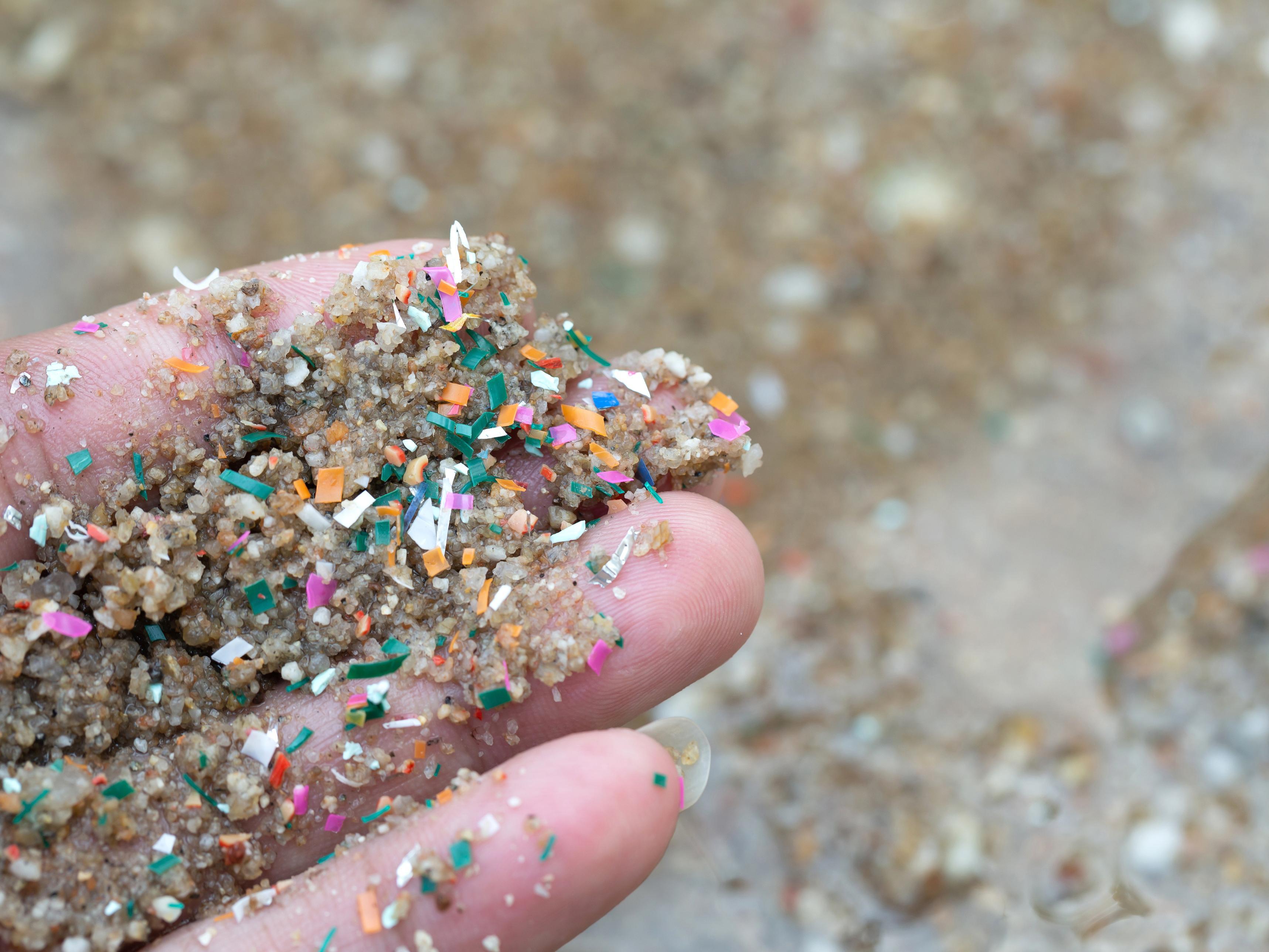 Eine Hand mit Sand und Mikroplastik.