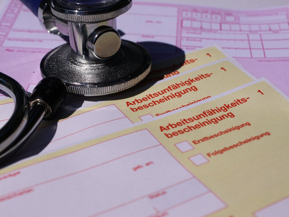 Das Foto zeigt ein Stethoskop, das auf einem Stapel Arbeitsunfähigkeitsbescheinigungen liegt.